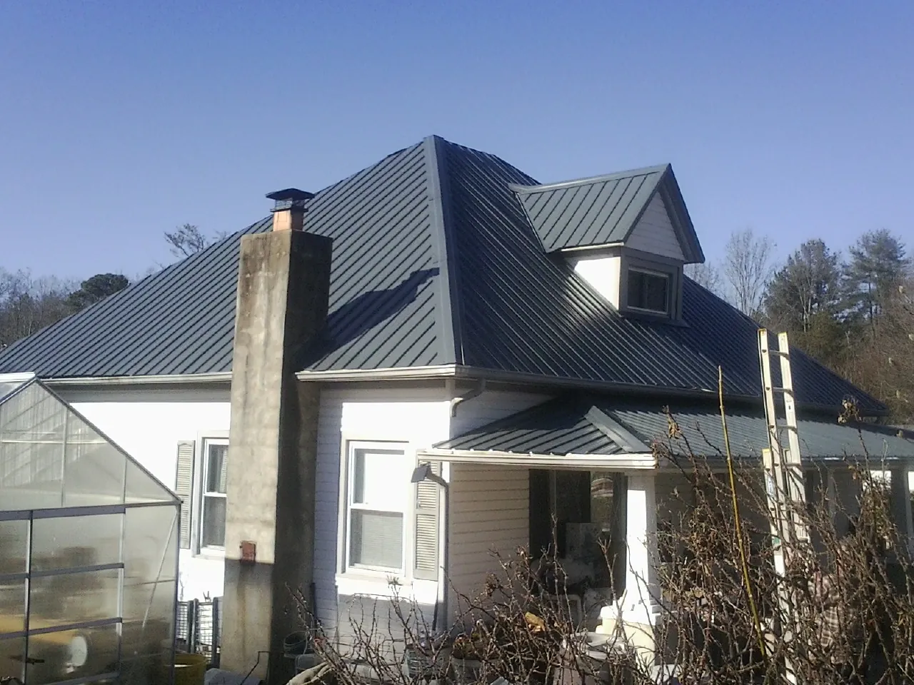 Dark blue standing seam metal roof on a white farmhouse with dormer — Slate & Tile Roof Repair by Roofing Brothers in Big Arm