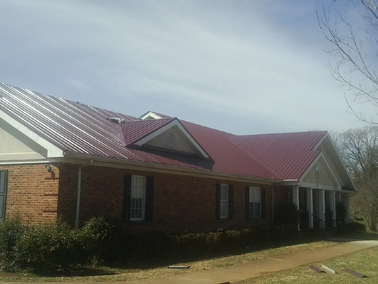 Red metal roof with gabled entries on a long brick building, from a Hail Damage Roof Repair job in Big Arm