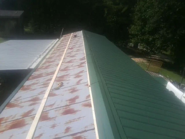 Old rusted panels beside newly installed green metal roofing — Wind Damage Roof Repair by Roofing Brothers in Big Arm