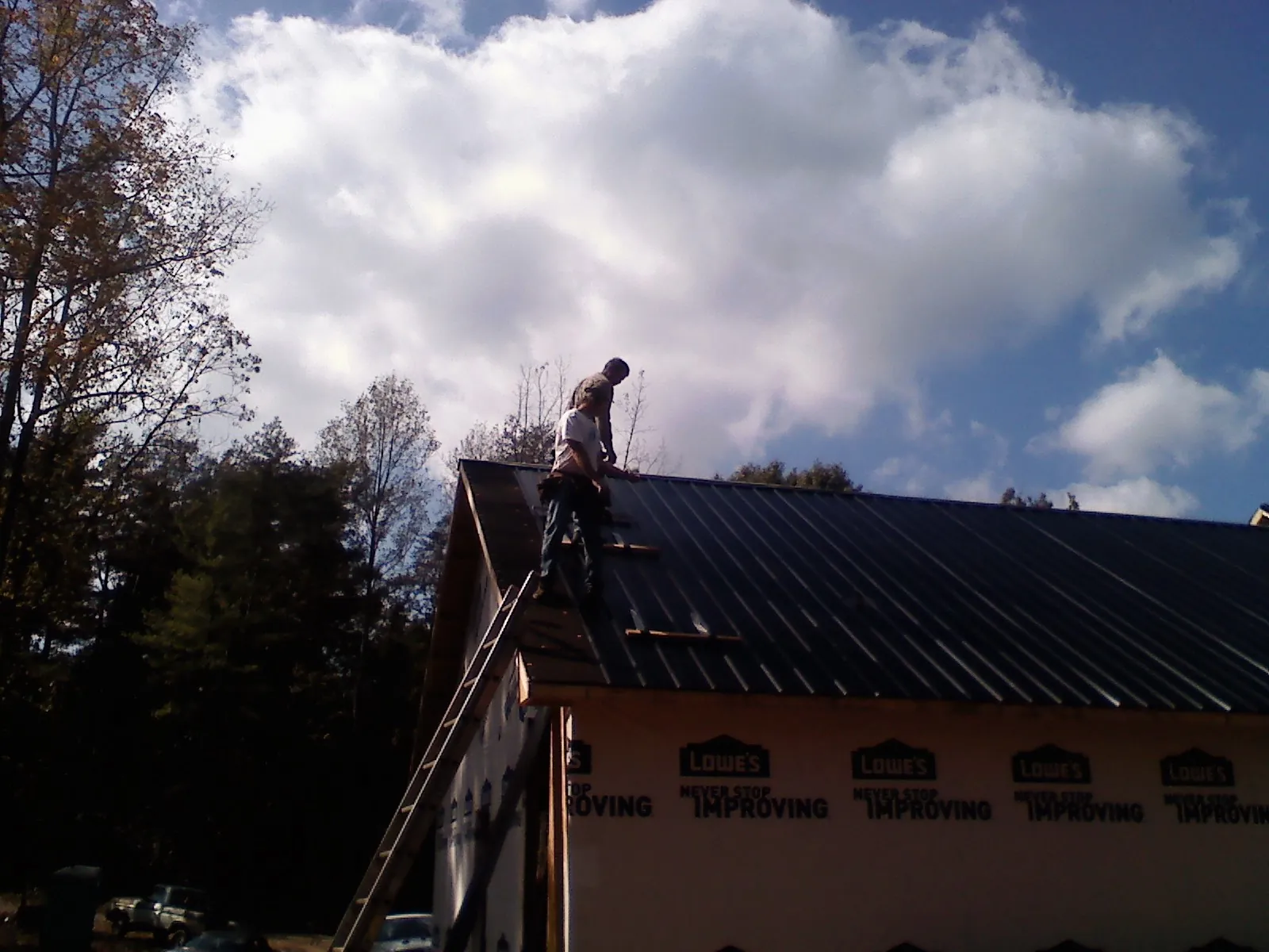 Roofer fastening dark metal panels high against a cloudy sky, from a Roof Inspection job in Big Arm