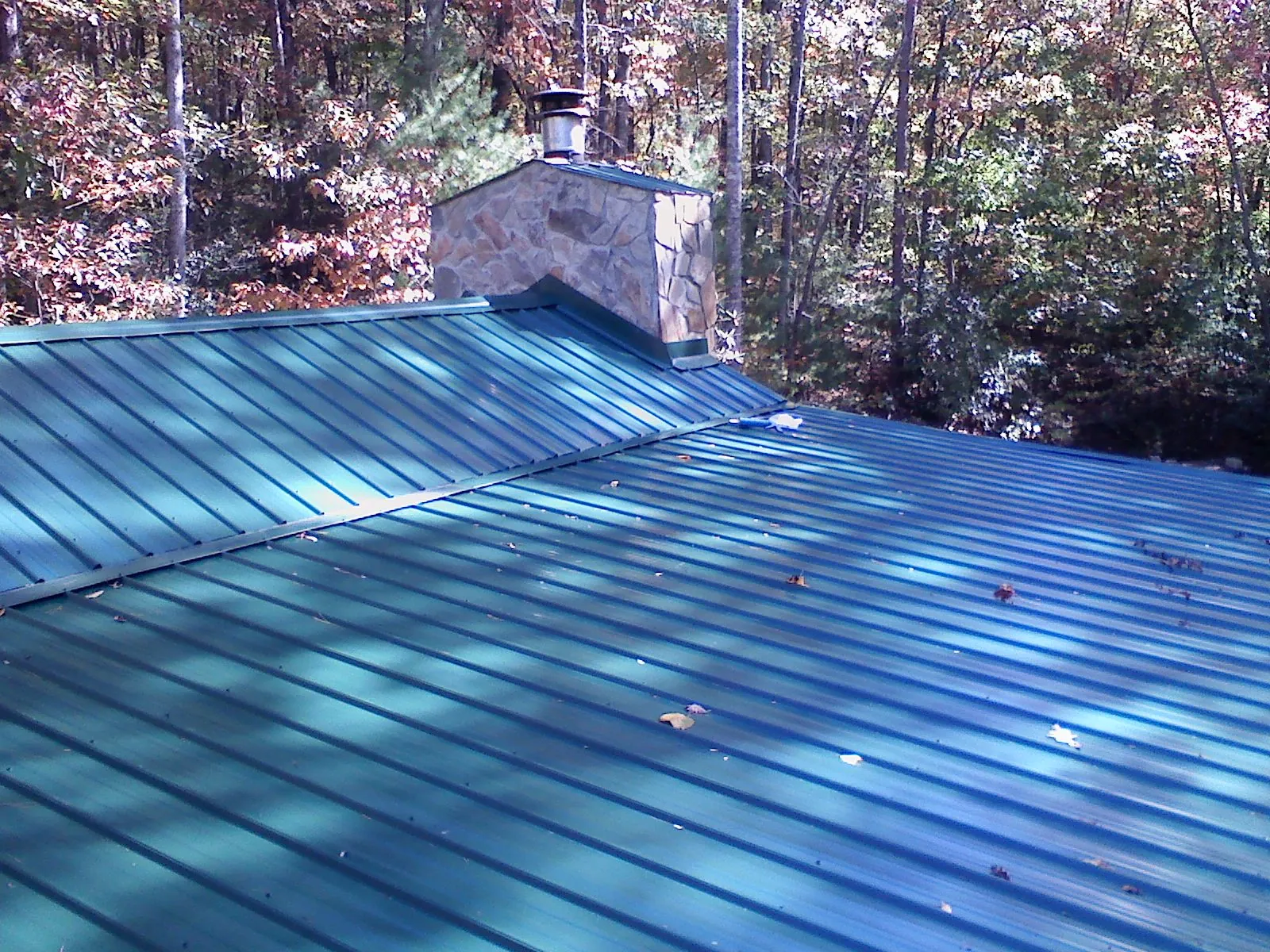New green metal roof and stone chimney surrounded by autumn woods in Big Arm