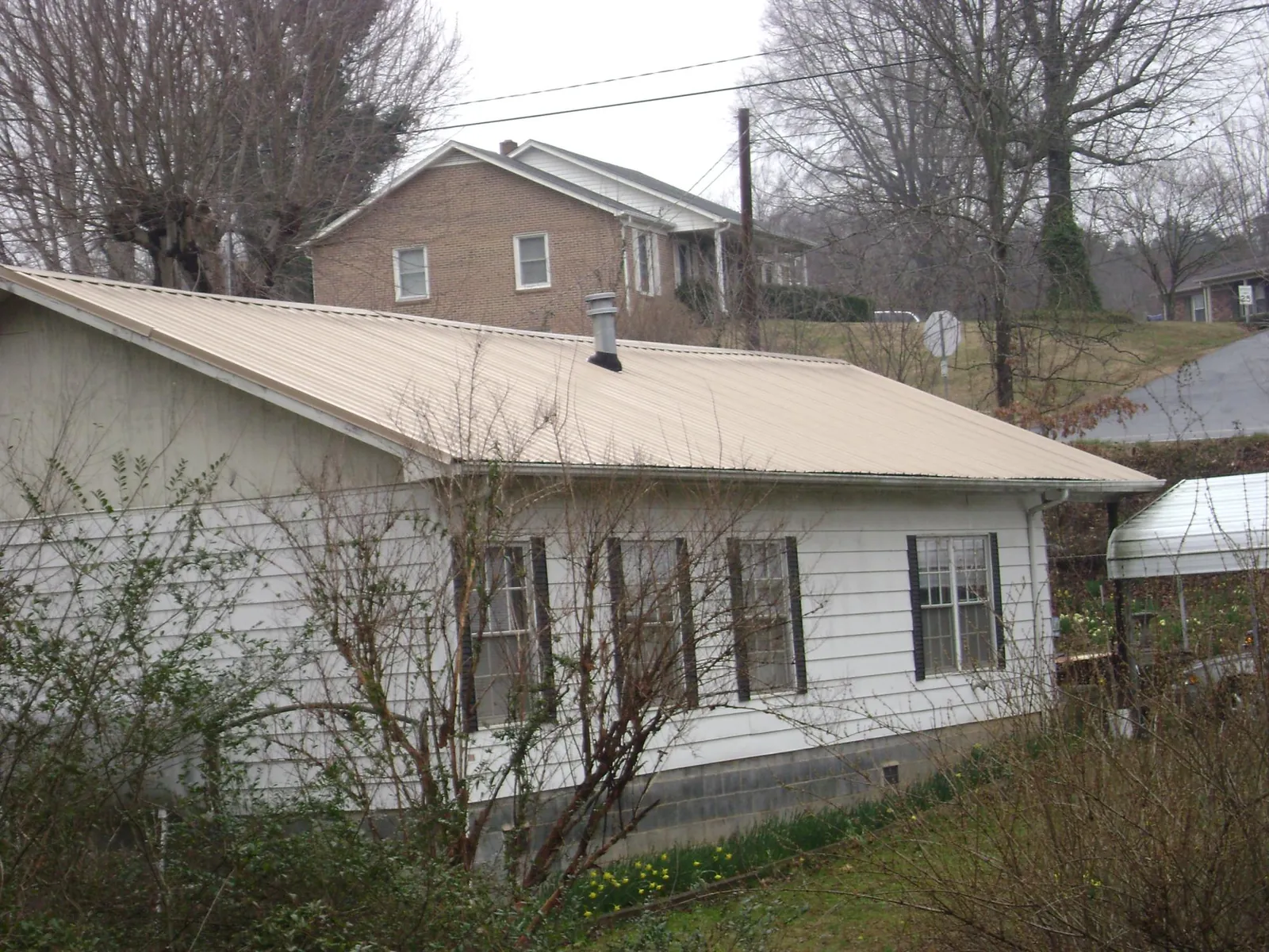 Tan metal roof on a white sided house set into a hillside — Commercial Roofing by Roofing Brothers in Big Arm